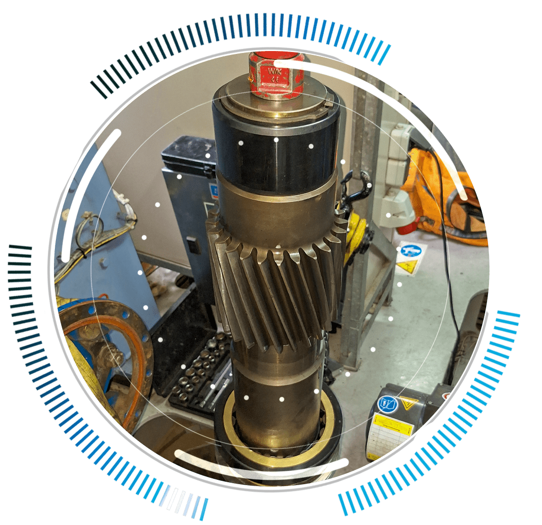 skywings.com.pl - A large cylindrical industrial gear mechanism with helical teeth, set up for Vestas-Getriebe-Service, stands vertically in a workshop. It is surrounded by circular blue digital graphic elements, with tools and equipment visible in the background. Wind Turbine Service & Maintenance, Windenergieanlagen-Service & Instandhaltung