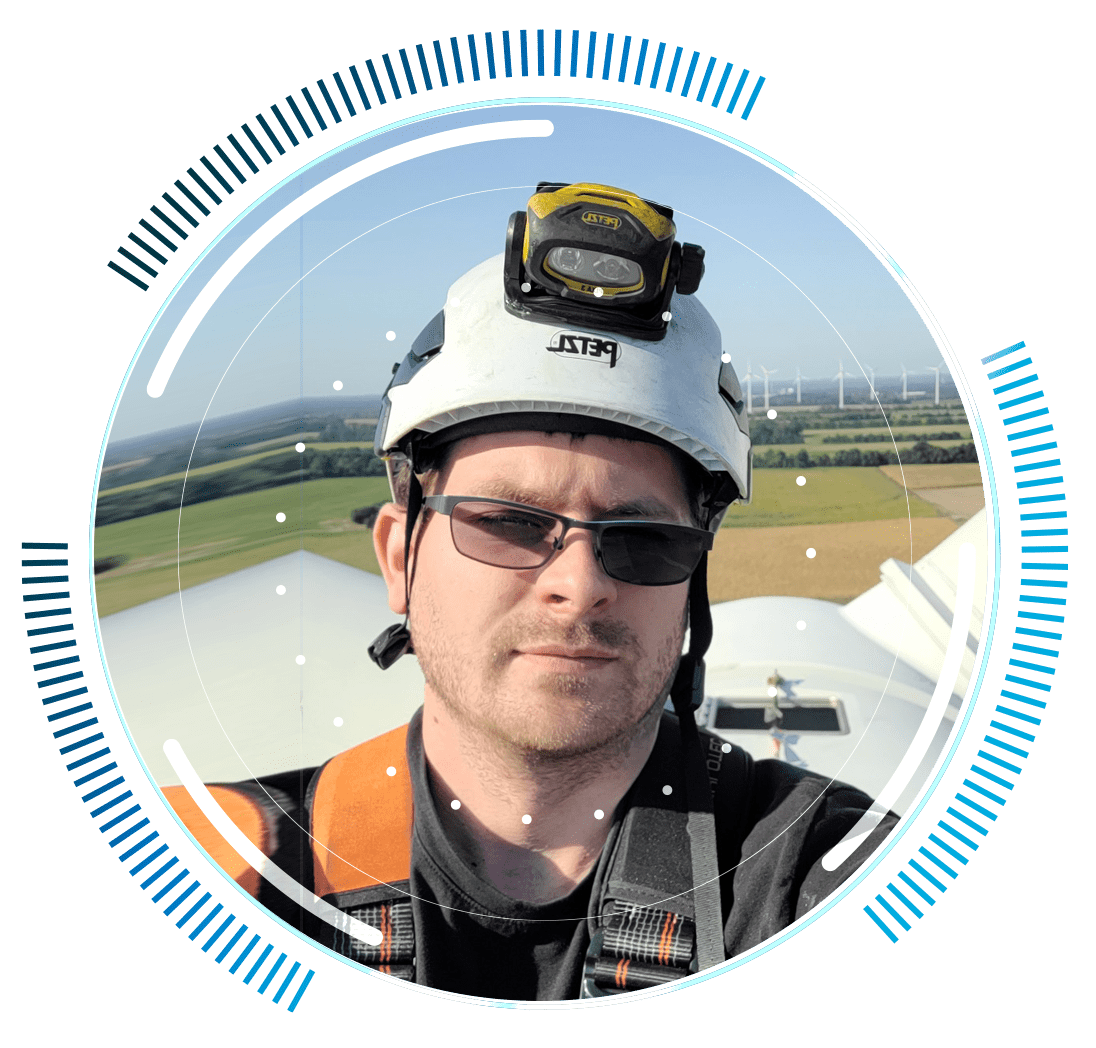 skywings.com.pl - A man wearing a helmet, headtorch, and sunglasses takes a selfie on top of a wind turbine after carrying out wind turbine electrical maintenance. Fields and wind turbines are visible in the background, with circular blue graphic elements framing the image. Wind Turbine Service & Maintenance, Windenergieanlagen-Service & Instandhaltung