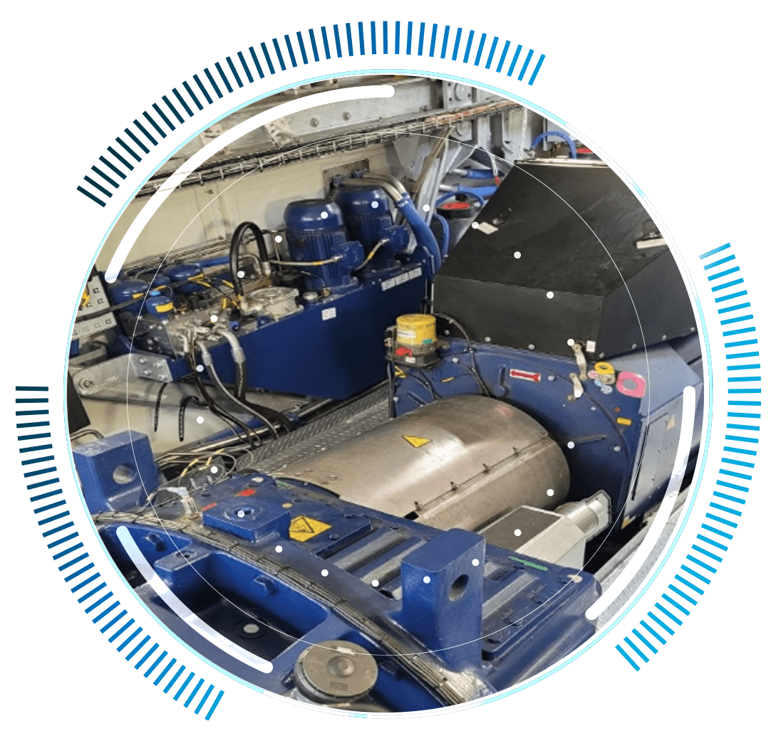 skywings.com.pl - Industrial machinery inside a factory, featuring large blue and silver metal components and hydraulic units—ideal for wind turbine hydraulic system servicing—with labelled warning signs and a circular digital graphic overlay framing the image. Wind Turbine Service & Maintenance, Windenergieanlagen-Service & Instandhaltung