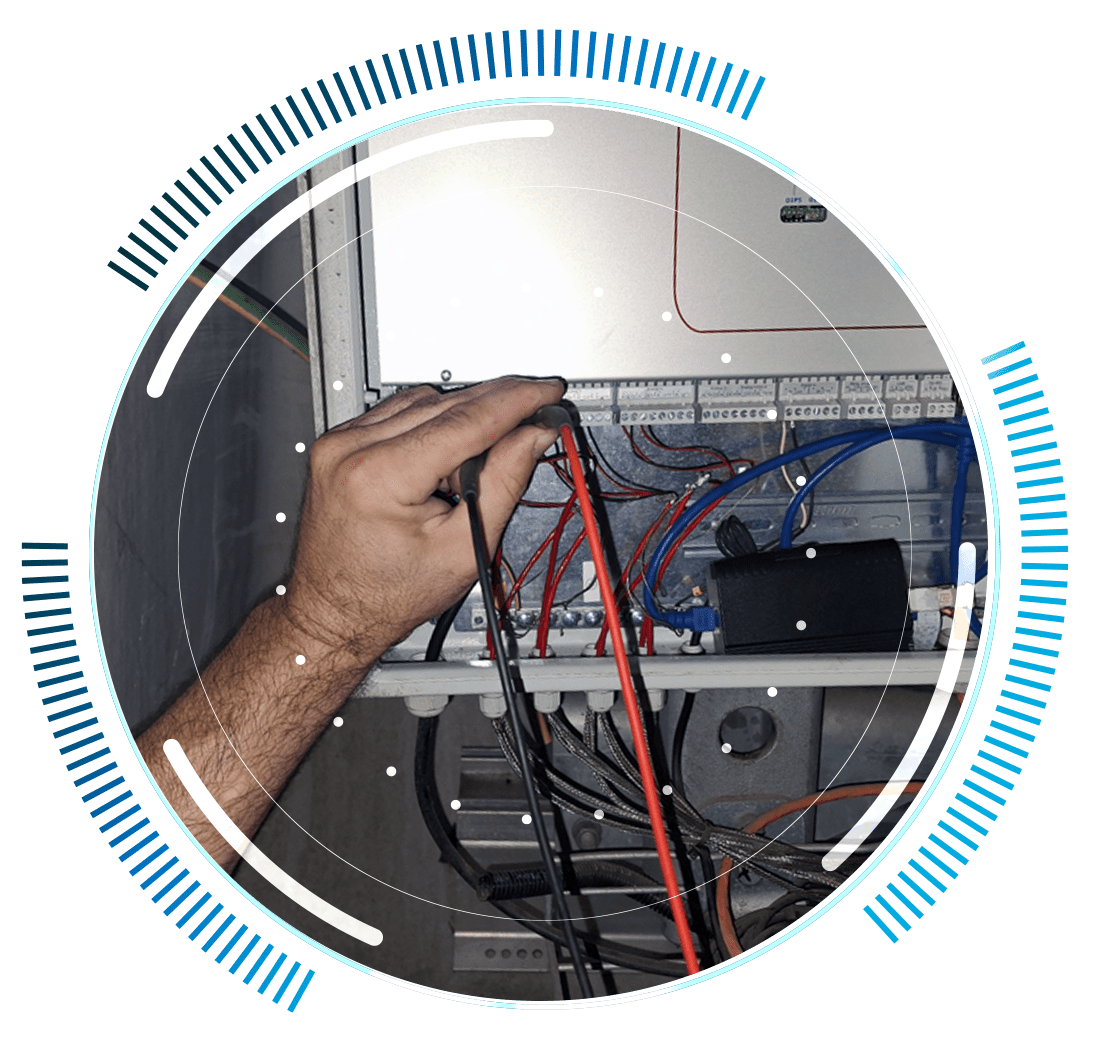 skywings.com.pl - A person’s hand holds red and black electrical testing probes to wires in an open electrical control panel, surrounded by a circular blue digital graphic overlay—highlighting the precision involved in wind farm technical service. Wind Turbine Service & Maintenance, Windenergieanlagen-Service & Instandhaltung